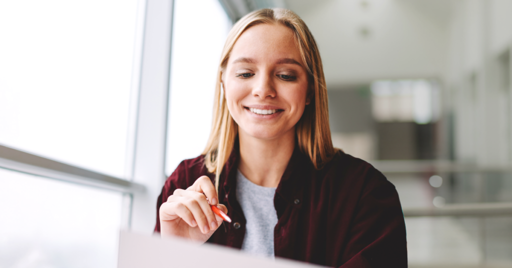 Woman smiling and holding a pen while ticking something off a list