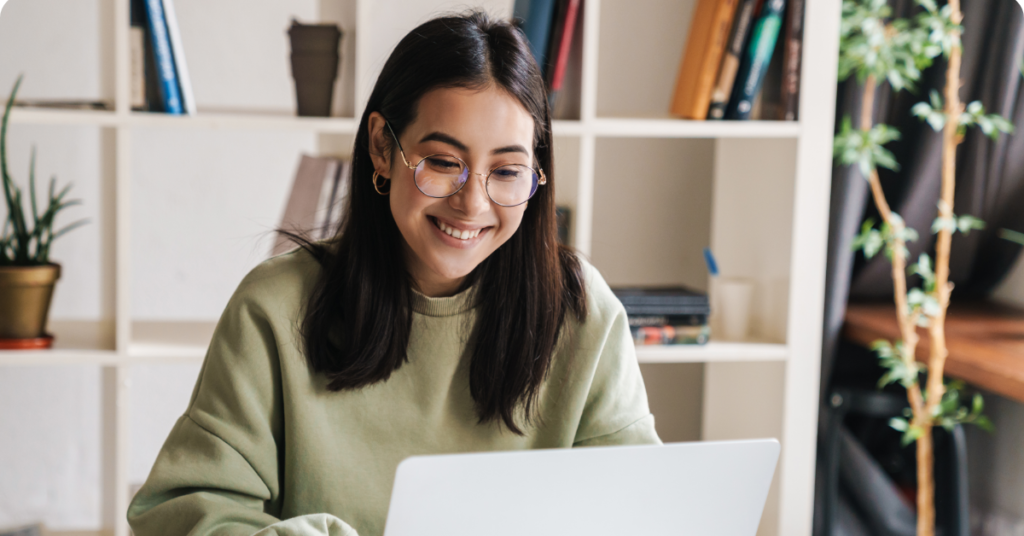 Young woman with glasses smiling at laptop