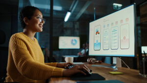 Woman smiling in front of a computer screen at desk | FourthRev